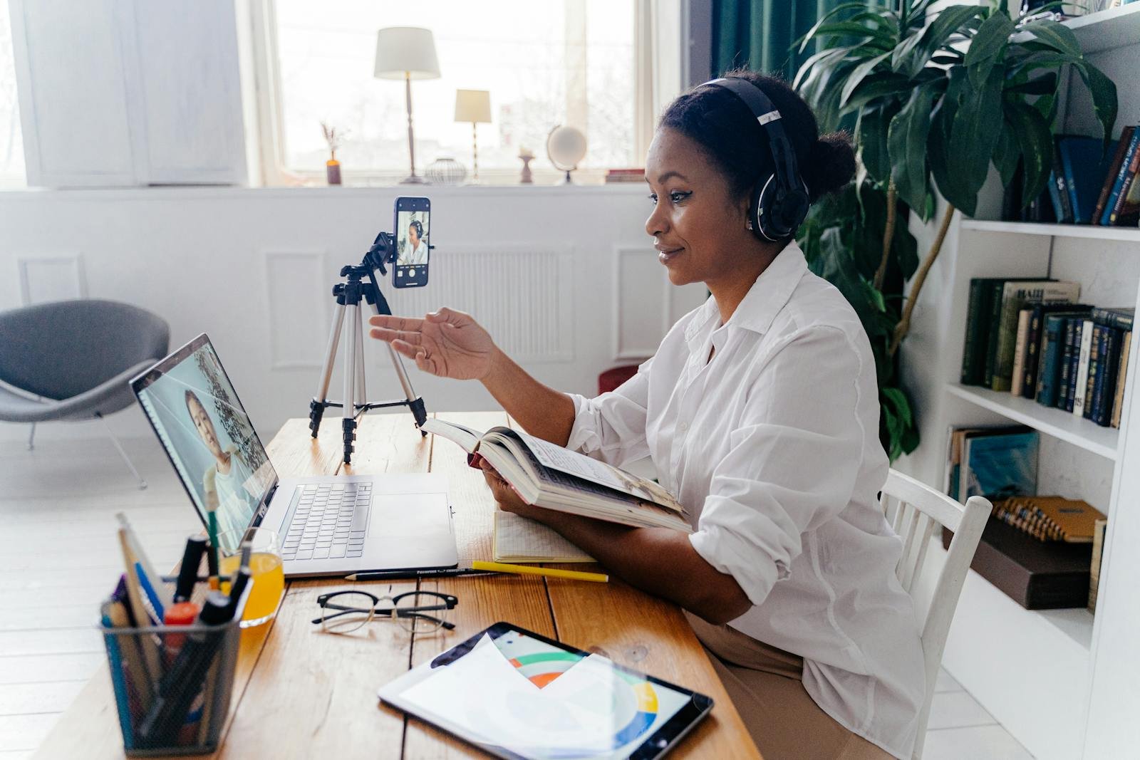 Comunicación Estratégica en la Era Digital, Woman engaged in a video conference, working remotely with laptop and tablet in a cozy home office.