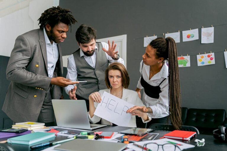 comunicación de crisis, Office scene with diverse colleagues around a stressed woman holding a sign that says 'HELP'. Focus on teamwork dynamics.