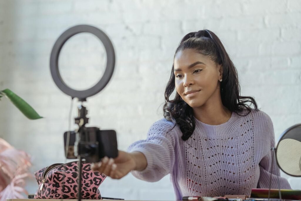 videos profesionales con tu celular, Glad African American female blogger with long dark hair using mobile phone and ring lamp while having video conversation online