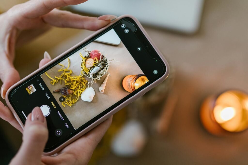 fotos profesionales con tu celular, Close-up of hands using smartphone to photograph seashells and candles.