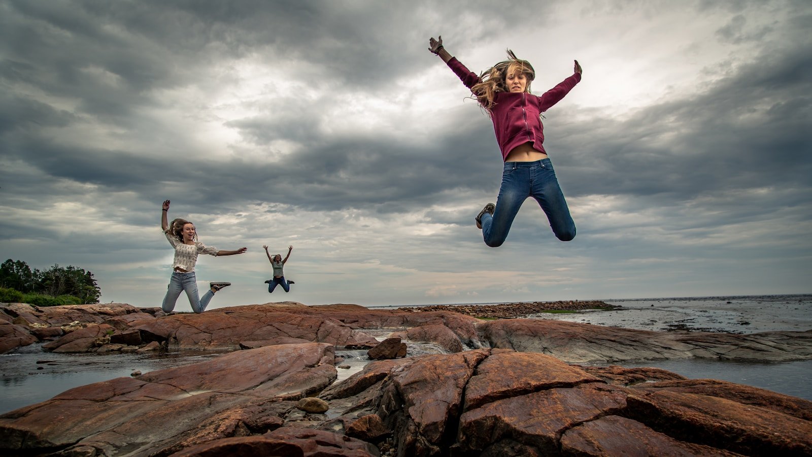 habilidades blandas esenciales, man in red and white jacket jumping on brown rock formation under cloudy sky during daytime