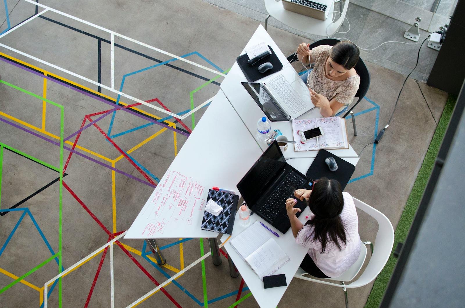 comunicación institucional para el 2026, Overhead view of women working together in a modern office setting with colorful geometric floor design.