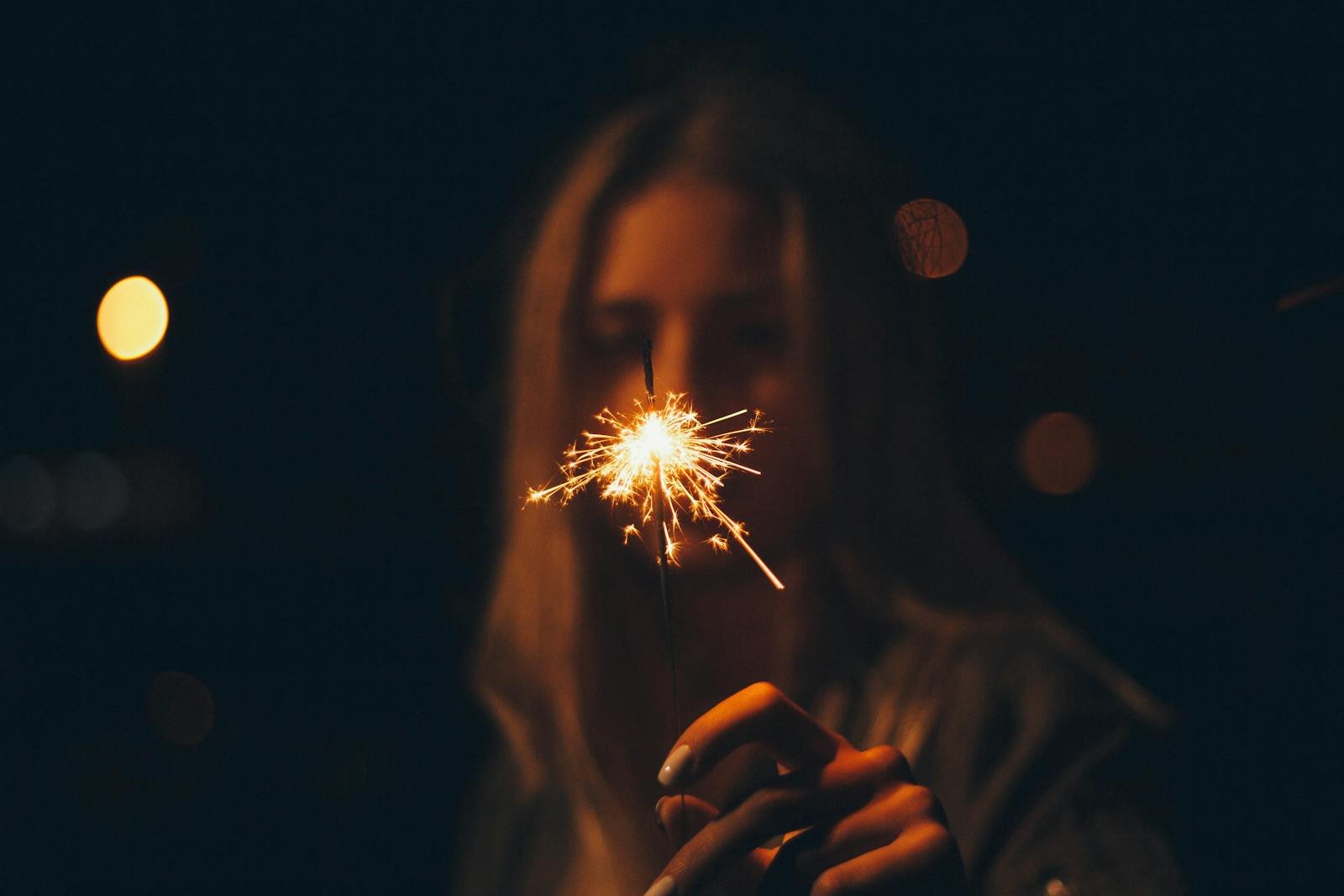 propósitos de año nuevo, A blurred image of a woman holding a bright sparkler in the night creates a warm, festive atmosphere.