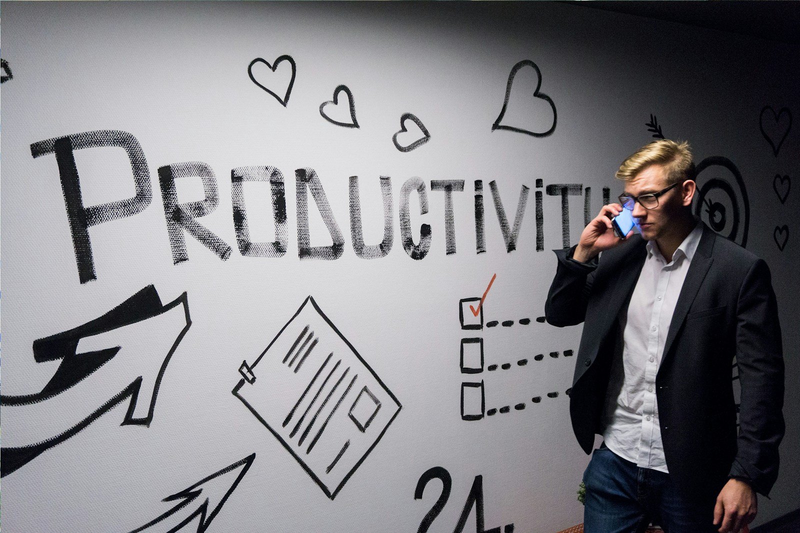metodologías de productividad, man holding smartphone looking at productivity wall decor