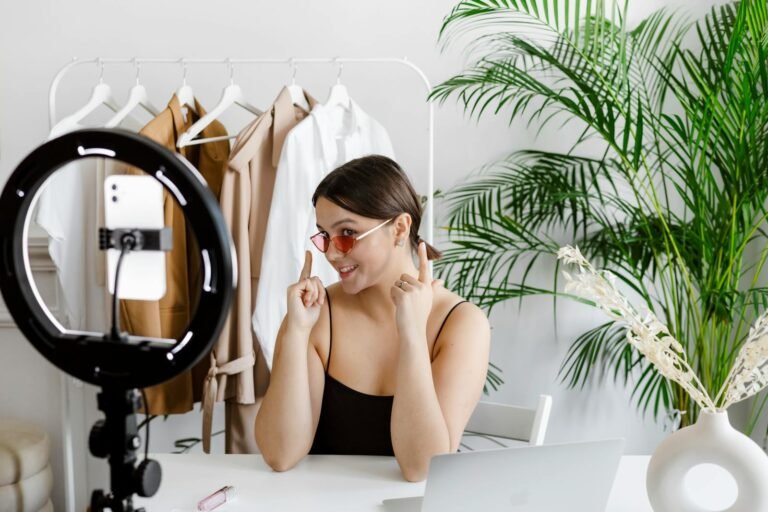marketing de contenidos, Stylish woman vlogging with ring light, surrounded by fashion accessories and greenery.