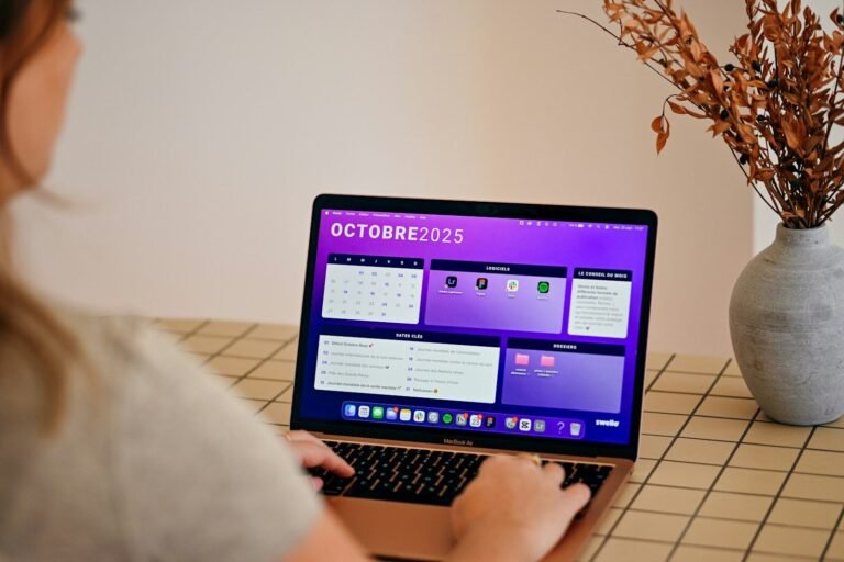 automatización de redes sociales, Woman using laptop with october 2025 calendar displayed.