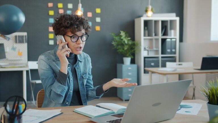 crisis reputacional, Woman talking on phone at desk with laptop.